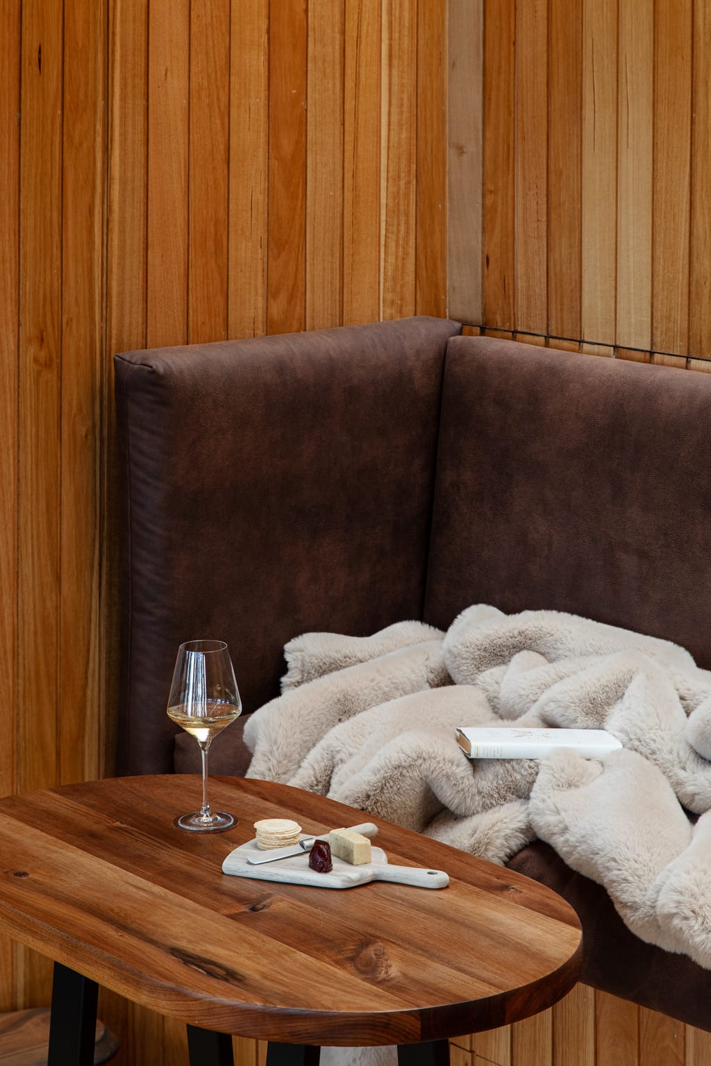 A cosy corner of a Hunter cabin: a leather banquette with a soft throw, a book and a glass of wine on a timber table