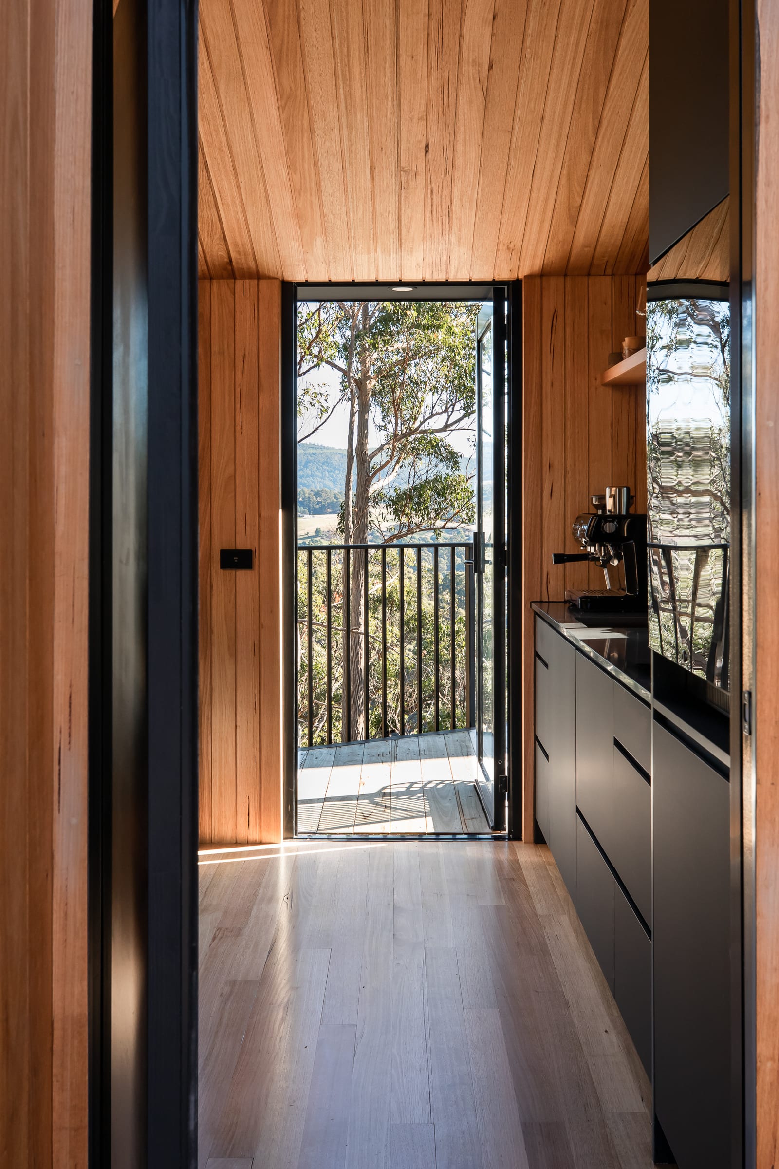 Inside a Hunter cabin, a timber galley kitchen opening onto a private deck with the valley beyond the glass door
