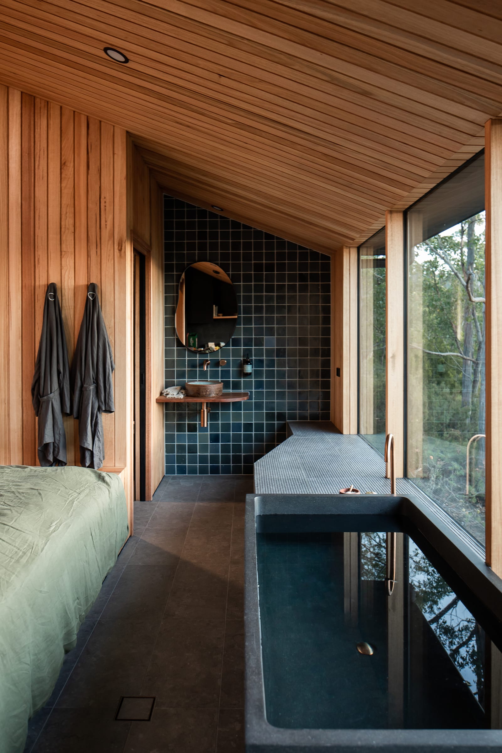 Inside a Hunter cabin, a deep black stone bath running along full-height windows beside a green-tiled ensuite
