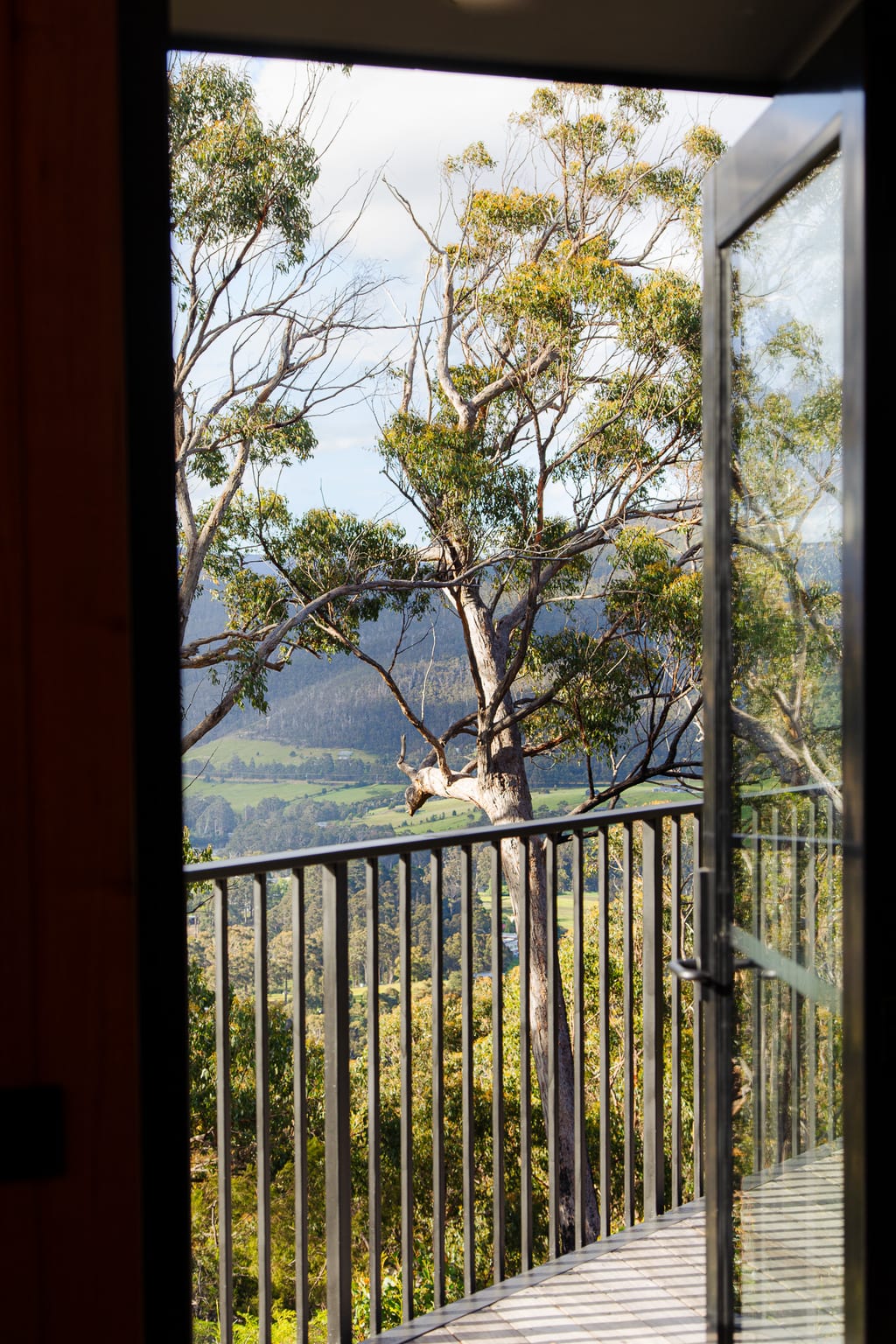 The view from a Hunter cabin doorway out over the Huon Valley, tall eucalypts and rolling farmland below