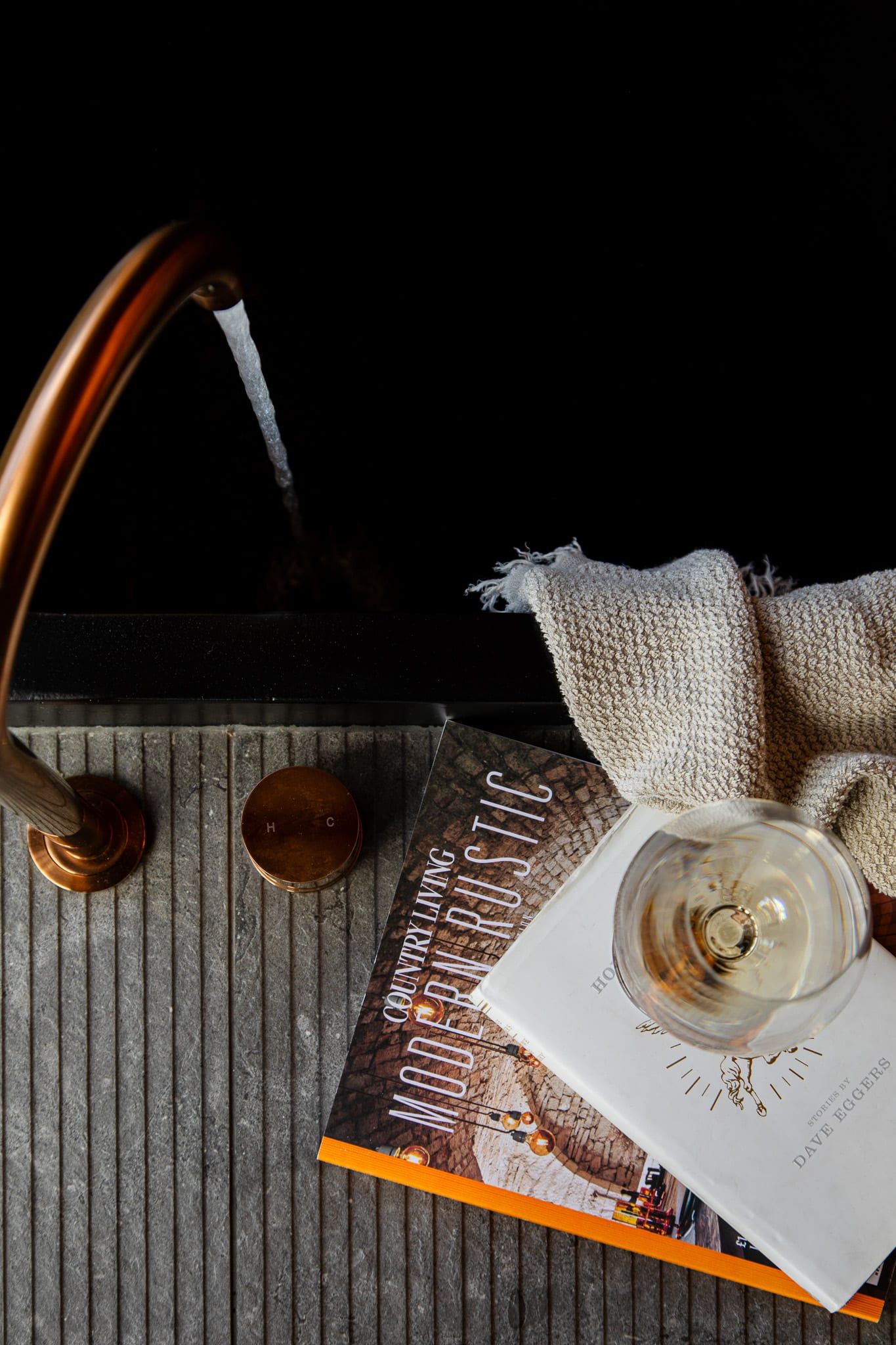 Water running from a brass tap into a Hunter cabin&rsquo;s stone bath, a book, a folded towel and a glass of white wine set out on the ledge