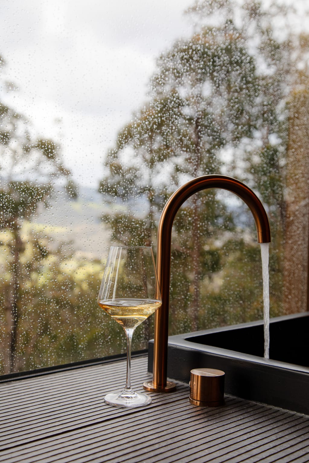 A glass of wine on the ledge of a deep stone bath as it fills with water inside a Hunter cabin