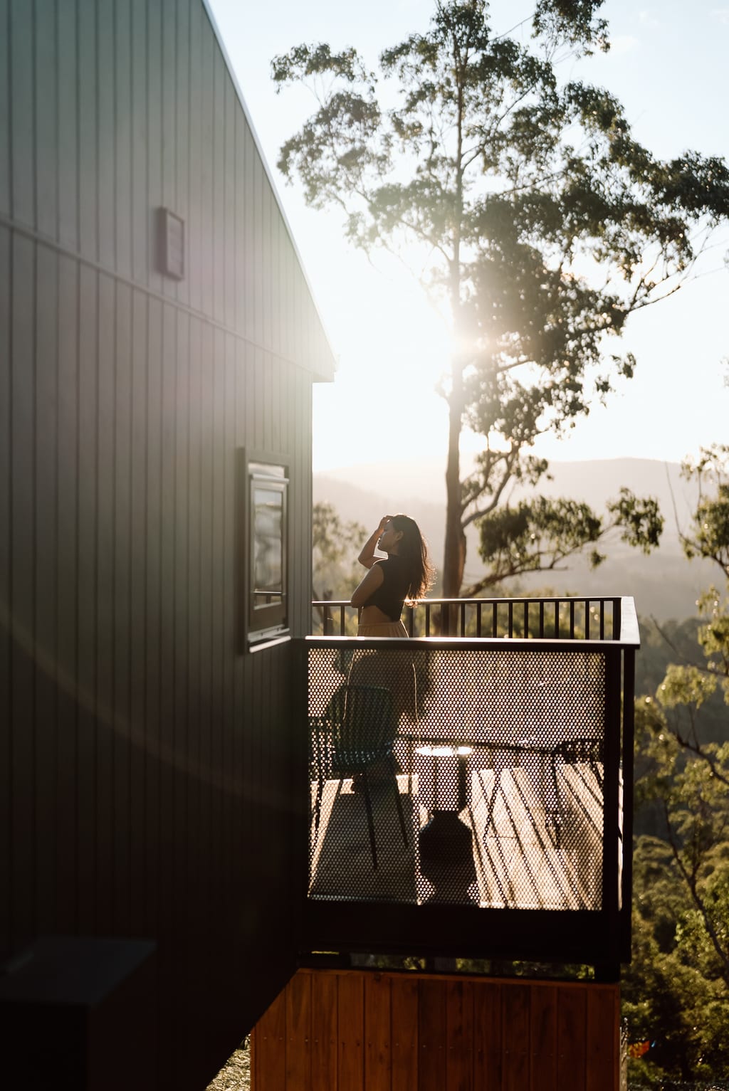 A woman standing on the timber deck of a Hunter cabin, looking out over the Huon Valley